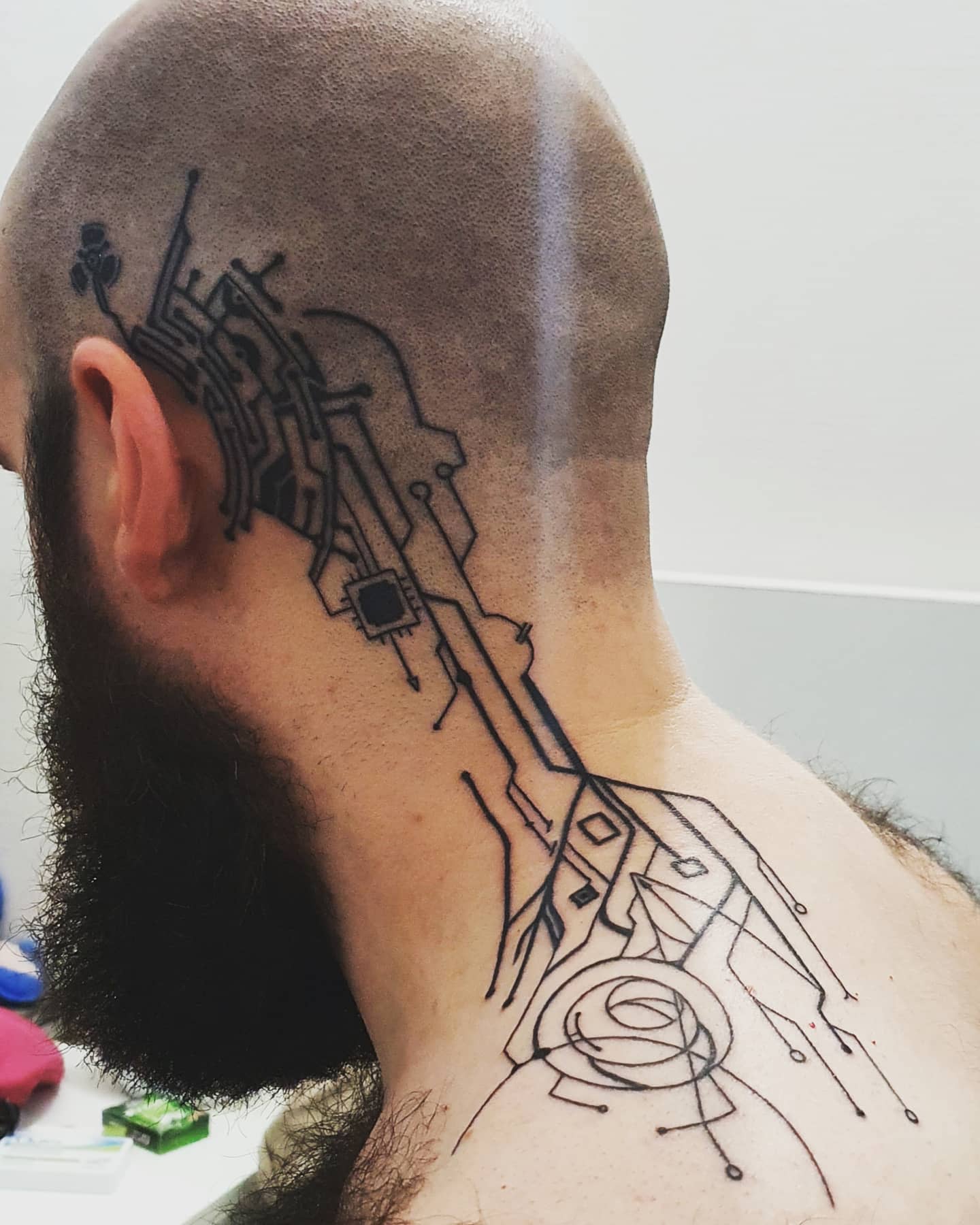 Geometric tech-inspired tattoo extending from the bald head down the neck